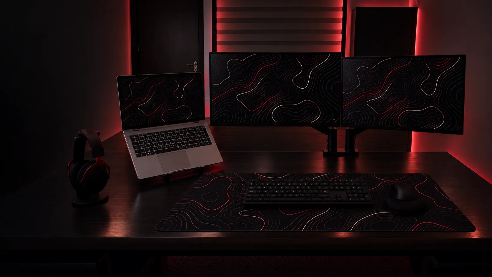 Issa Nijmeh’s workspace — a laptop and two monitors in a dark room lit deep red